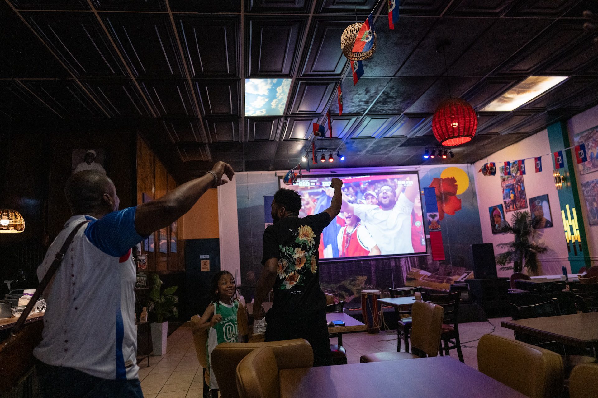 Adults and a child raise theirs arms in celebration while watching Haiti versus Morocco World Cup match a the Kinzin Creole restaurant.