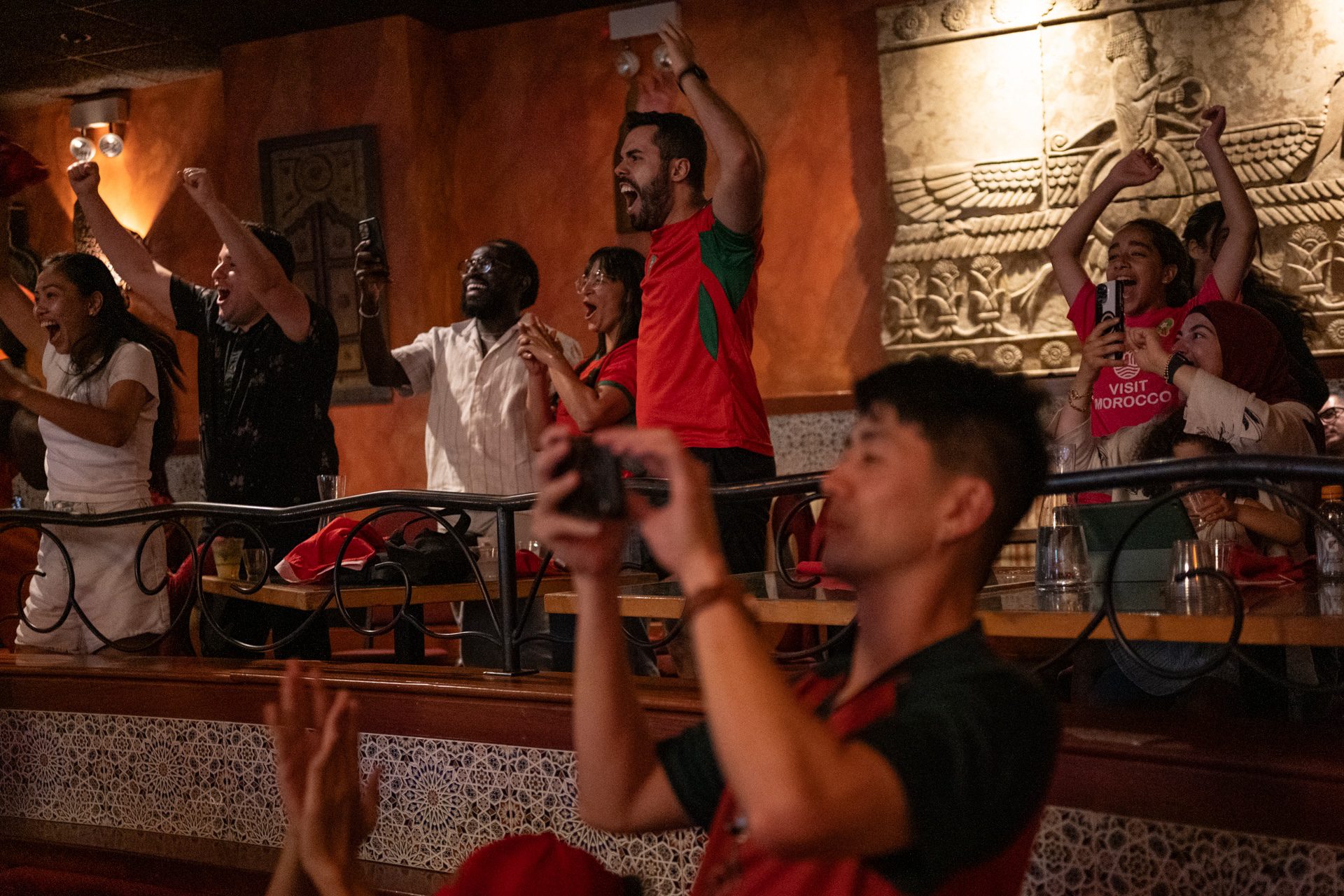 Fans stand up, raising their fists as they celebrate Morocco scoring their third goal against Canada during a World Cup viewing event at Alhambra Palace.