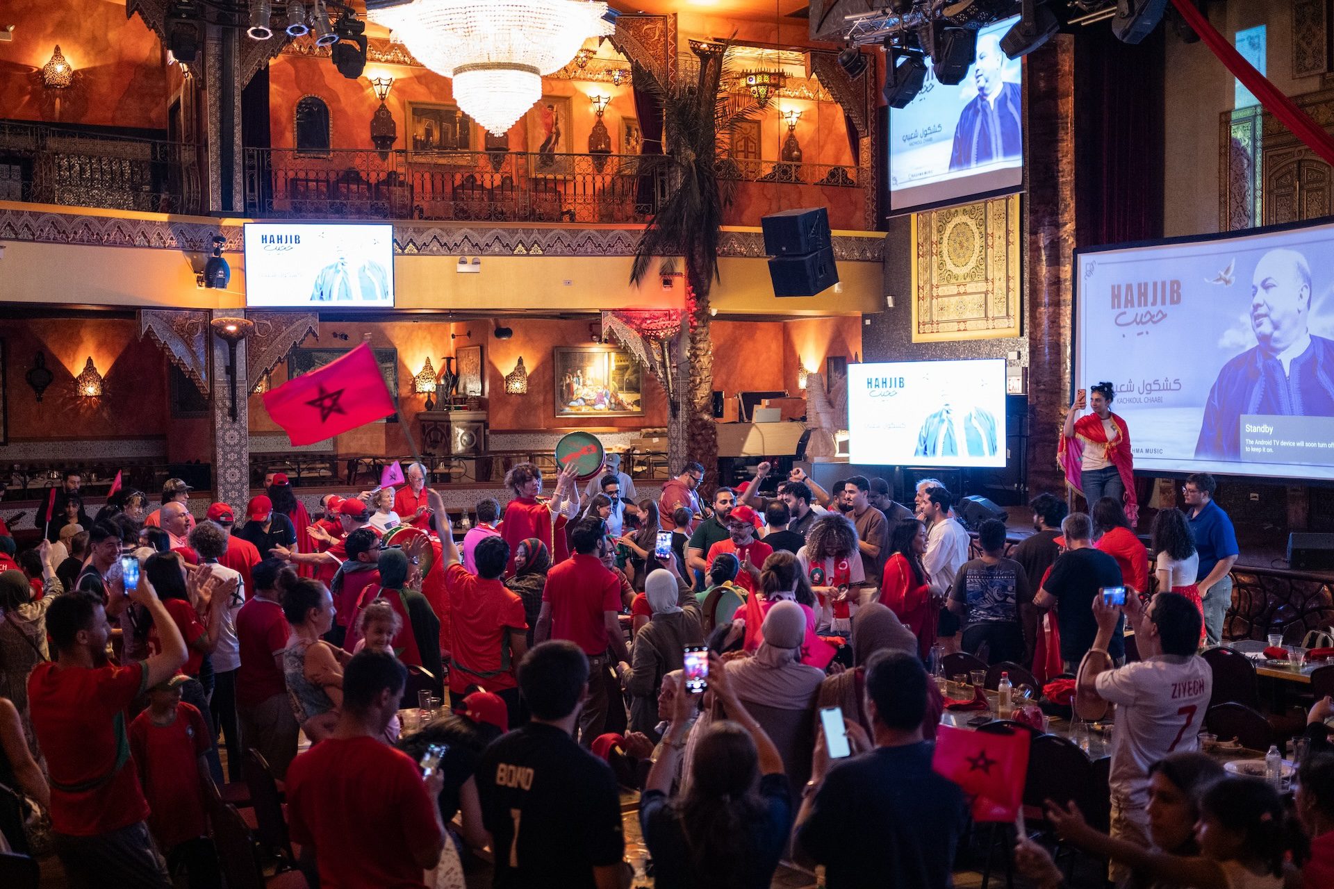 A large crowd of fans, many wearing red, celebrate Morocco's victory over Canada in the spacious restaurant, Alhambra Palace.