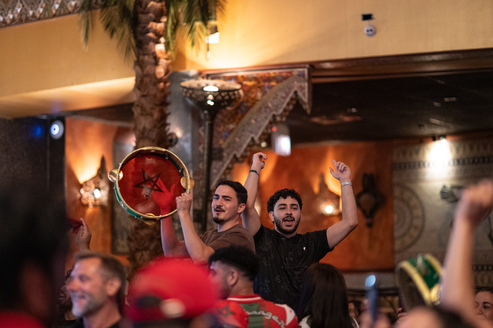 Two Fans raise their arms and a Tamborine as they celebrate Morocco's victory over Canada.