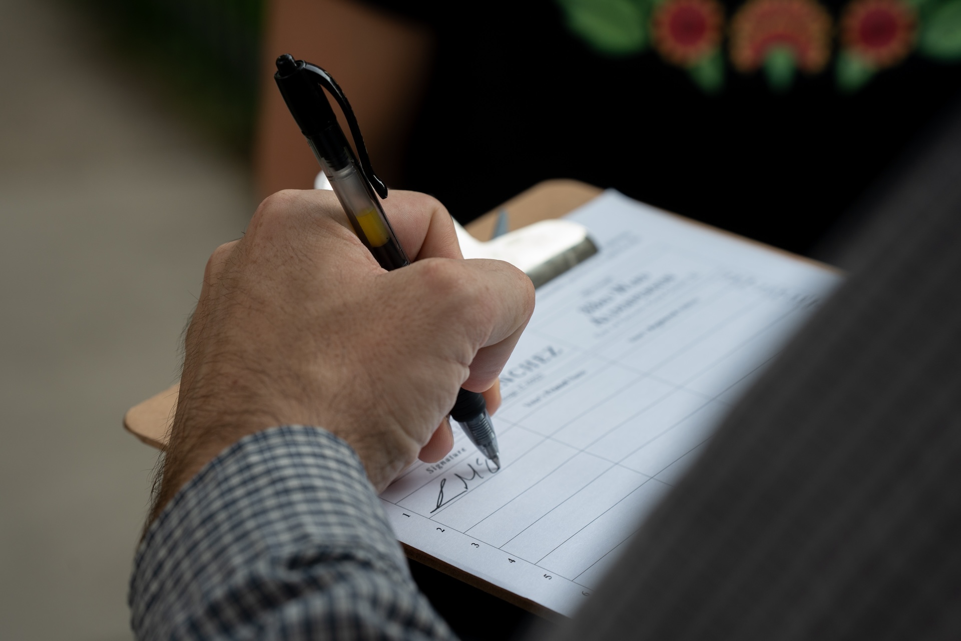 A close-up photo shows Ian McCullum signing a nominating petition for incumbent 33rd Ward Alder Rossana Rodriguez Sanchez in Albany Park on August 4, 2026.