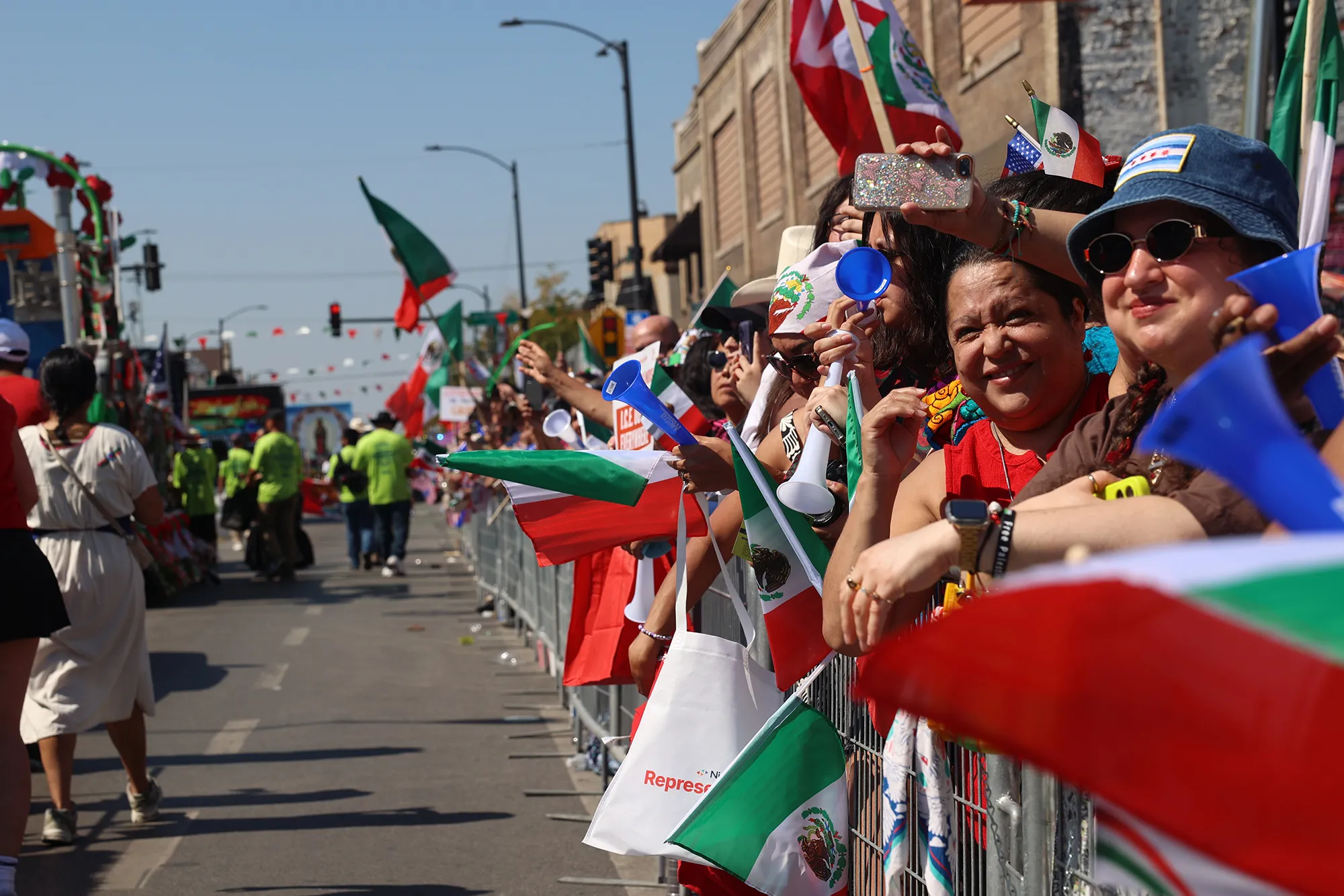 People standing behind metal barricades smile as they watch the start of the 54th annual 26th Street Mexican Independence Day Parade in Little Village on Sept. 14, 2025.