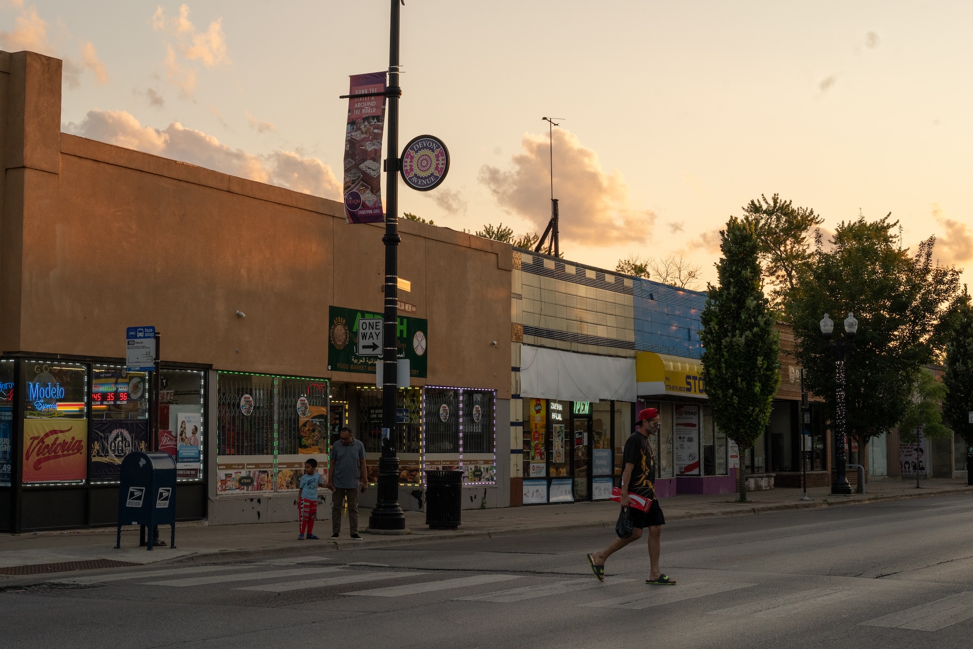 A pedestrian crosses Devon Avenue as the sun sets on the business district.