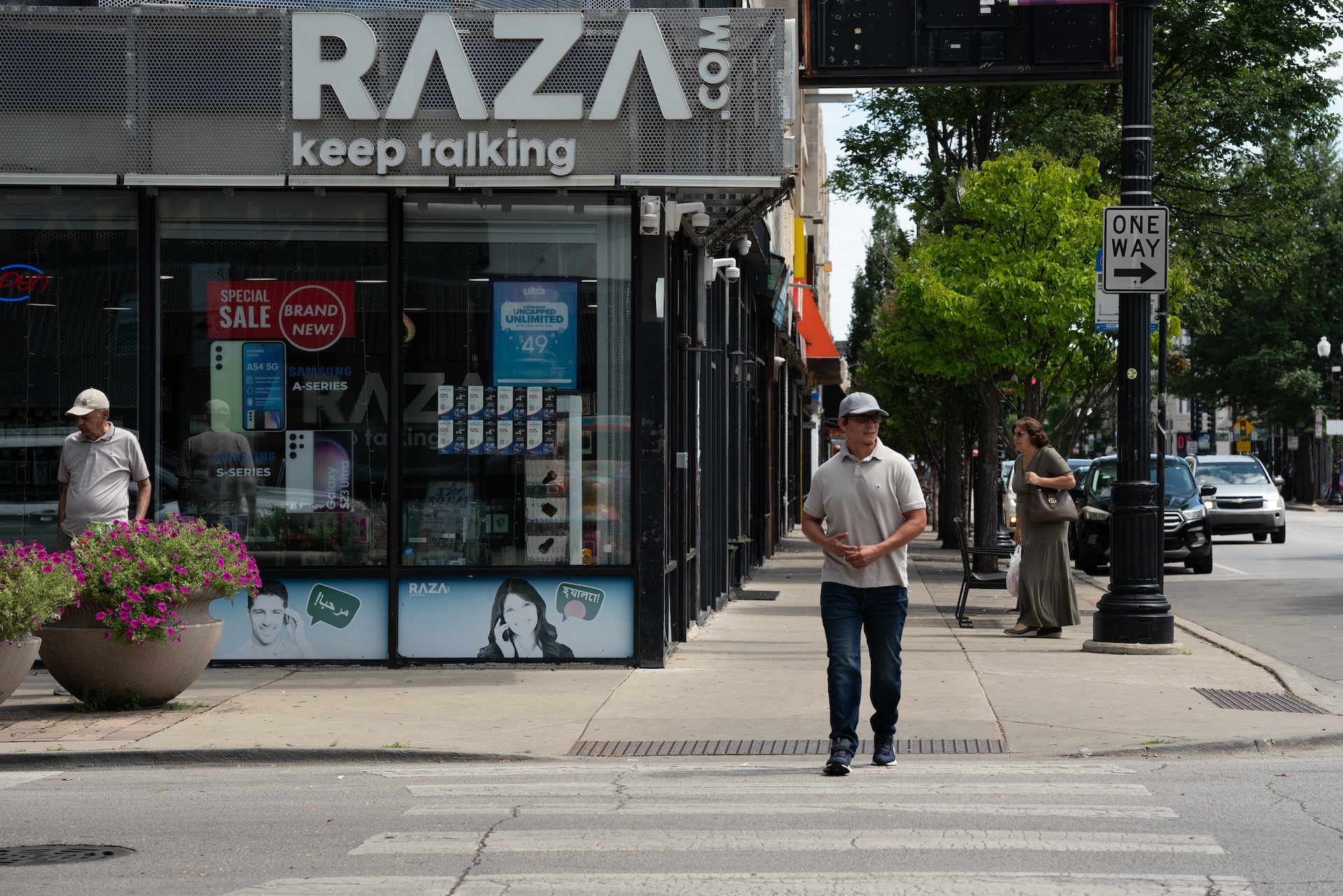 People walk on Devon and Campbell Avenues in front of a Raza.com Telecom store on a sunny day.