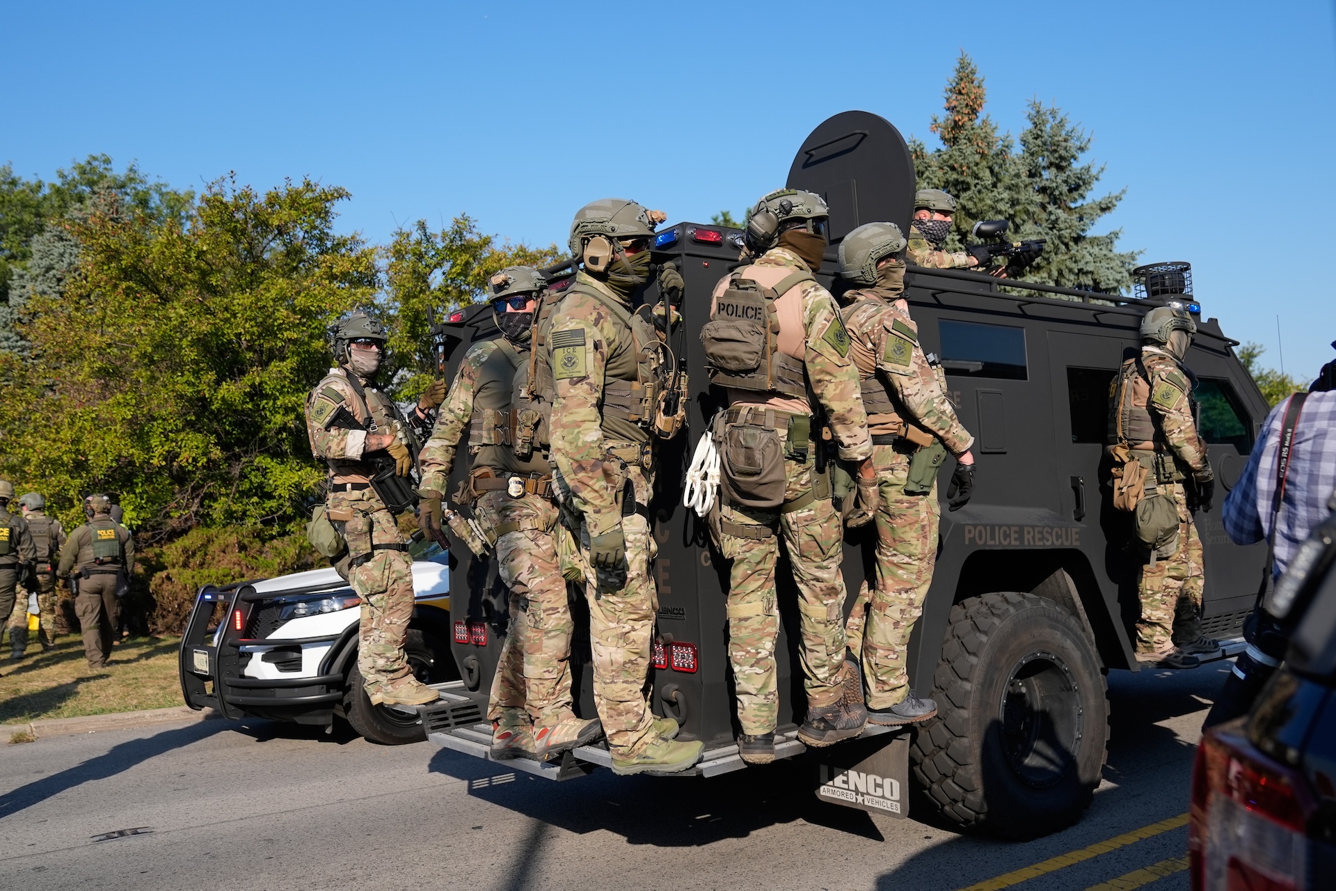 ICE agents arrive at an immigration and customs facility hanging onto an armored vehicle.