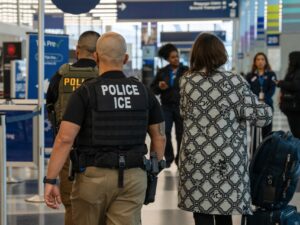 Two ICE agents wearing body armor vests walk alongside travelers at O'Hare International airport.