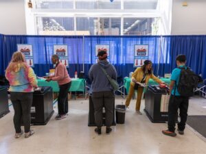 Three voters are assisted at voting kiosks by poll workers at the Chicago Voting Supersite.