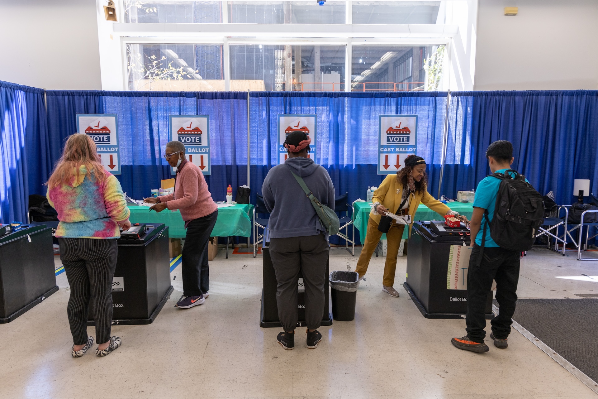 Three voters are assisted at voting kiosks by poll workers at the Chicago Voting Supersite.
